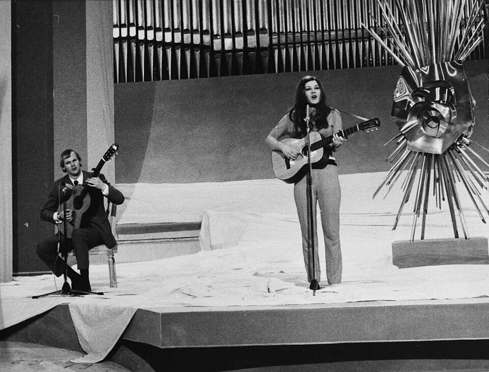 Lenny Kuhr singt mit Gitarre auf der ESC-Bühne 1969 in Madrid, links ihr Gitarrist Piet Souer