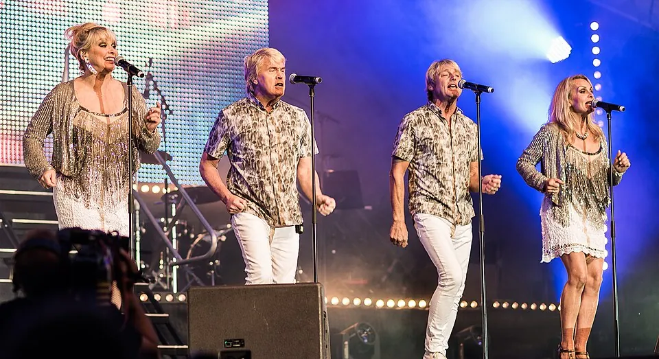 Die vier Mitglieder von Bucks Fizz singen an Mikrofonständern auf einer Bühne in Stockholm, 2015