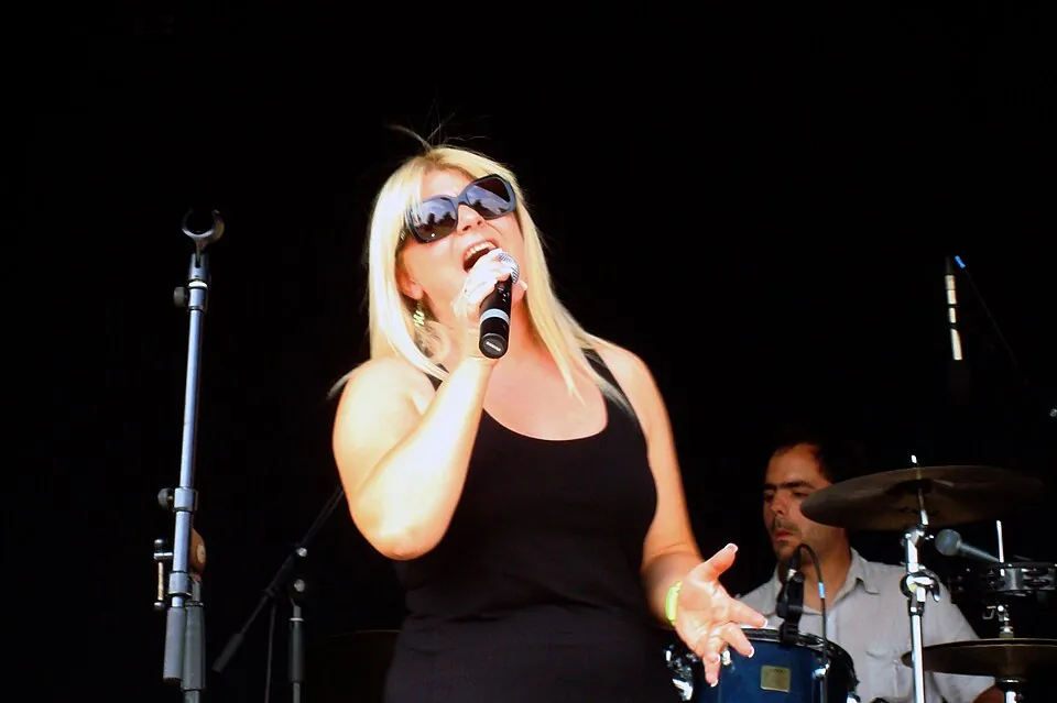 Sandra Kim mit Sonnenbrille singt beim Soundcheck auf einer Bühne, im Hintergrund ein Schlagzeuger, 2011