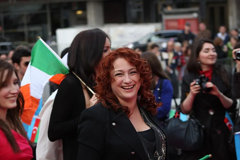 Lachende Niamh Kavanagh mit roten Locken und irischer Flagge bei der ESC-Eröffnungsfeier in Oslo 2010