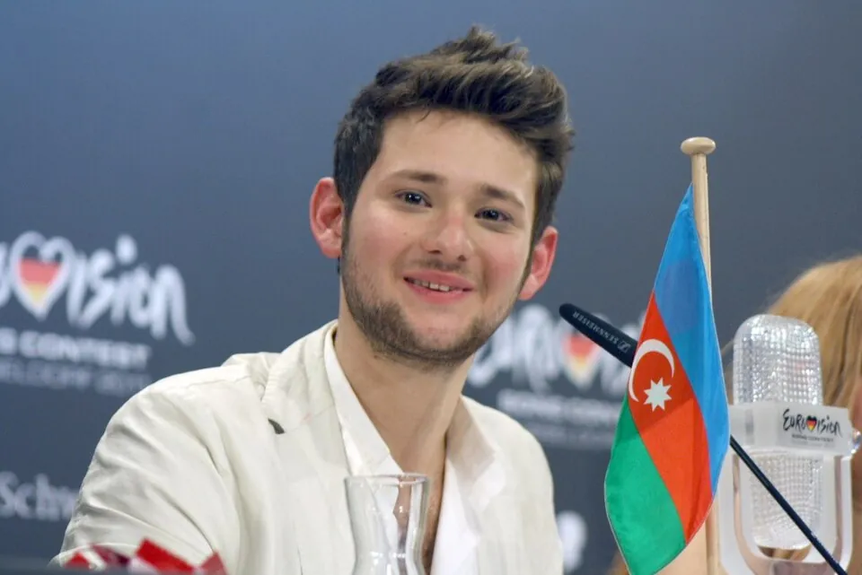 Lächelnder Eldar Gasimov bei einer ESC-Pressekonferenz 2011, neben ihm die Flagge Aserbaidschans