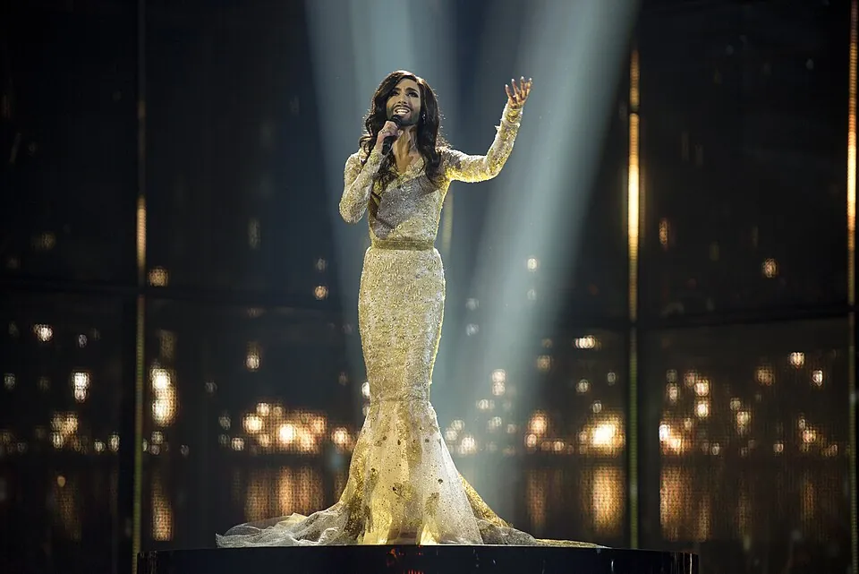 Conchita Wurst im goldenen Abendkleid singt mit erhobenem Arm im Scheinwerferlicht, ESC 2014