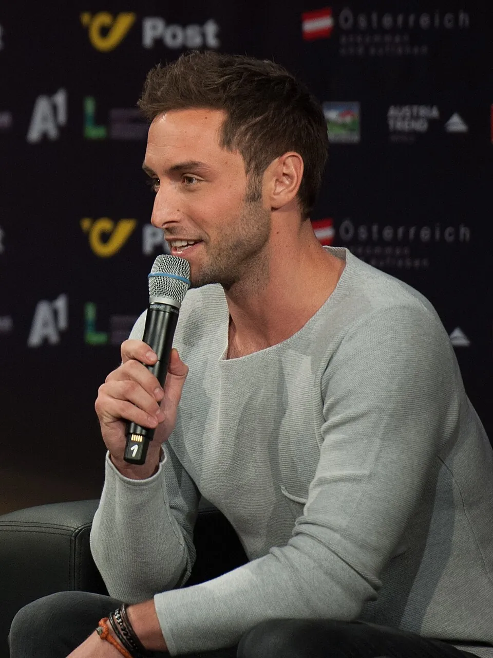 Måns Zelmerlöw im grauen Pullover spricht mit Mikrofon bei einer Pressekonferenz des ESC 2015