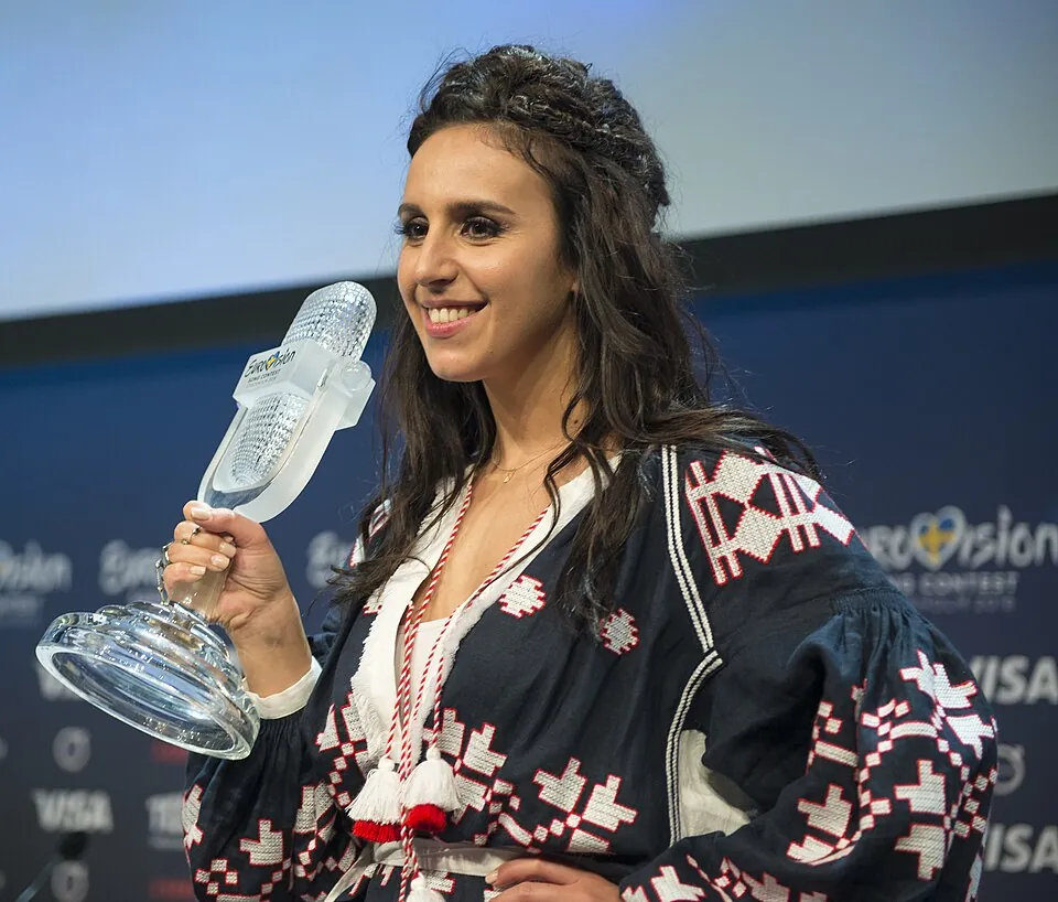 Lächelnde Jamala im bestickten Kleid hält die gläserne Mikrofon-Trophäe, Sieger-Pressekonferenz 2016