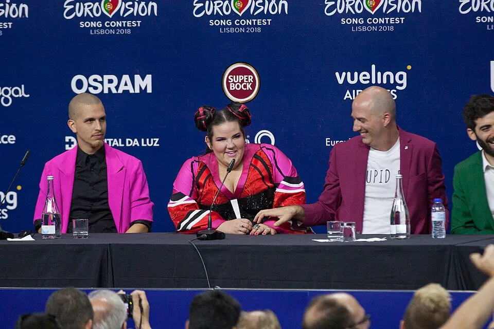 Netta mit Haarknoten sitzt lächelnd zwischen ihrem Team am Tisch der Sieger-Pressekonferenz 2018