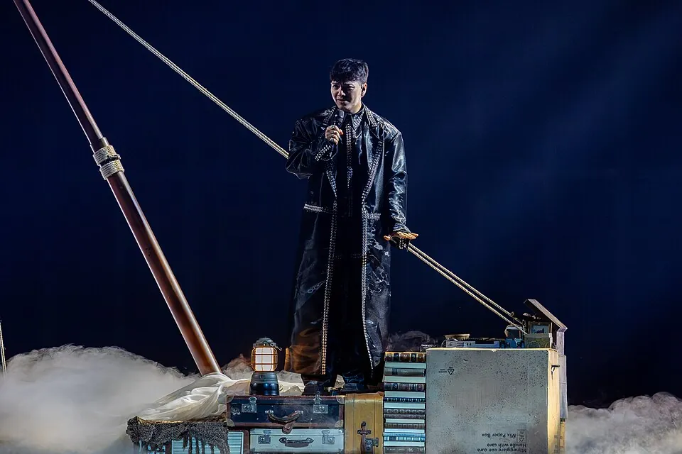 JJ im langen dunklen Mantel singt auf einer Schiffsdeck-Kulisse zwischen Koffern und Nebel, ESC 2025